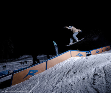 Snowboarder mid air about to hit the rail at night Snowboarder mid air about to hit the rail at night