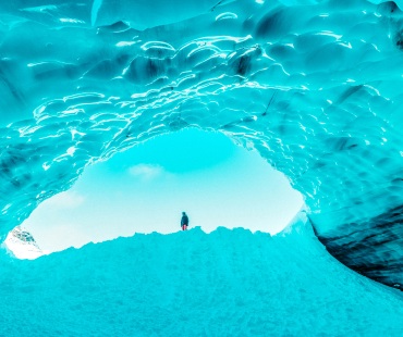 ethereal blue ice caves with skier standing in the opening ethereal blue ice caves with skier standing in the opening