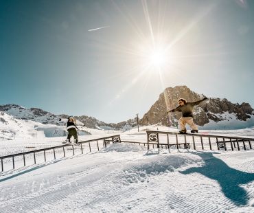 Two snowboarders boardsliding rails Two snowboarders boardsliding rails