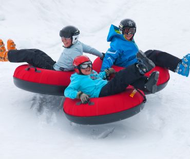 3 People riding tubes down snowy trails 3 People riding tubes down snowy trails