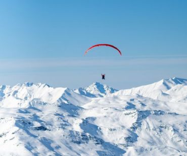 Person paragliding over the snow covered mountains Person paragliding over the snow covered mountains